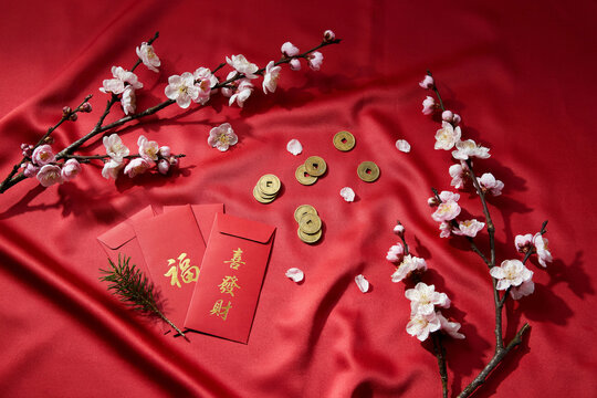 Chinese New Year flat lay on red silk fabric, red envelope with gold characters, lucky coins and cherry blossom branches for festive greeting design