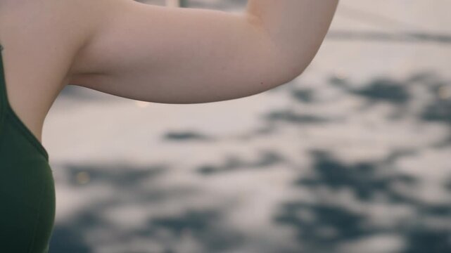 Close up of woman stretching her arm with soft lighting and shallow depth of field. subject wears dark green sports bra revealing upper body tattoo on shoulder blade while wearing fitness