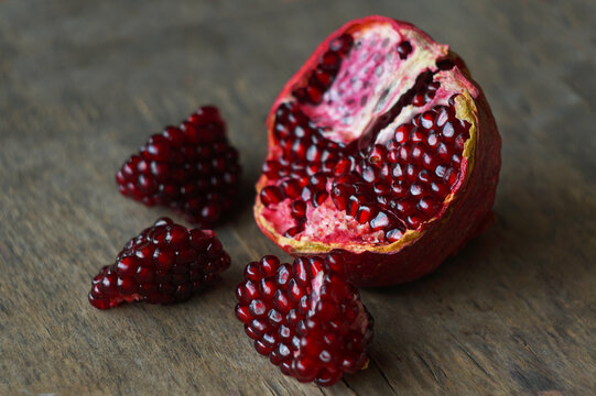 Half cracked open ripe pomegranate with fresh ruby red seed chunks on a wooden background.