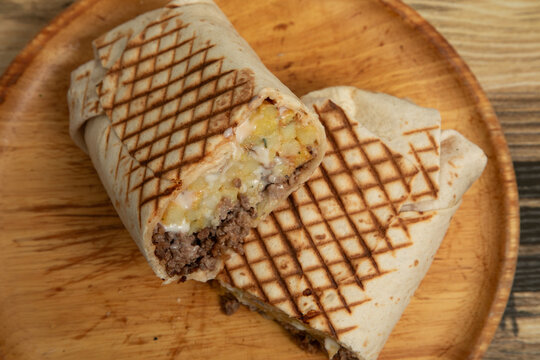 Tacos fran&ccedil;ais coup&eacute; en deux garni de viande hach&eacute;e, frites et sauce fromag&egrave;re sur planche en bois