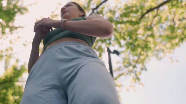Close up of young woman performing leg stretches outdoors in daylight wearing casual athletic wear and smartwatch. Her movements show flexibility training with visible fabric texture details