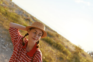Naklejka premium A young woman with braided hair wearing a straw hat and striped polo shirt enjoys the summer sun during a peaceful outdoor lifestyle moment in the golden hour.