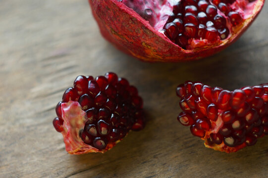 High angle shot of ripe pomegranate chunks with ruby red seeds on a wooden table.