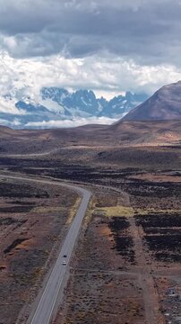Scenic road through the vast arid landscape of Patagonia, Argentina, with snow-capped mountain peaks in the background under a cloudy sky