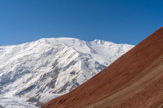 North face of Lenin Peak under clear blue sky in Kyrgyzstan as seen from Travelers Pass with red slope in the foreground 