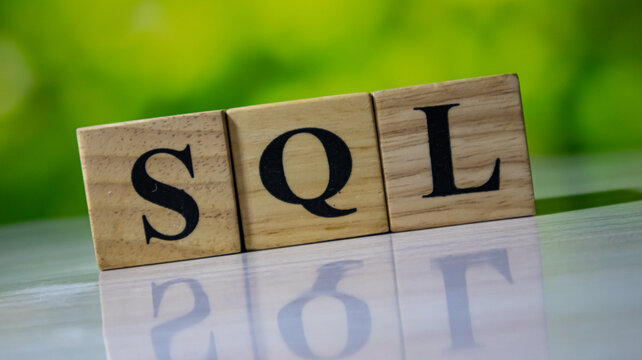 SQL wooden blocks spelling on white table with green bokeh background.