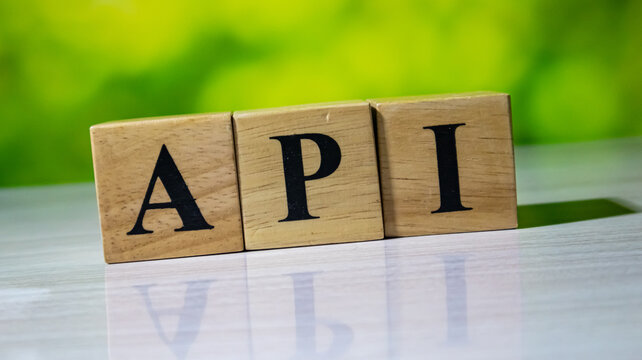 API acronym printed on wooden blocks resting on white tabletop with green background.