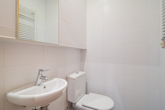 Bright modern bathroom with white toilet wall-mounted sink and mirrored cabinet in tiled interior