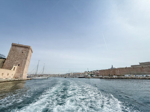 Panoramic view of Marseille's Vieux Port from the water, with the harbor entrance, historic stone fortifications, marina masts and city skyline surrounding the old Mediterranean port in Provence.