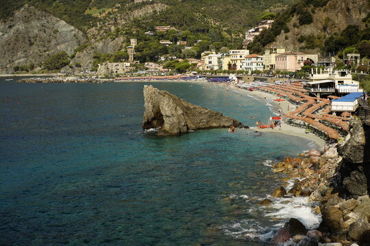 Spiaggia di Monterosso al Mare con scoglio, ombrelloni arancioni e mare turchese