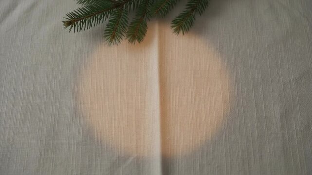 Warm circular light expands on a textured linen tablecloth with a pine sprig