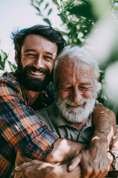 Handsome man and his father smiling in the garden, hugging each other.