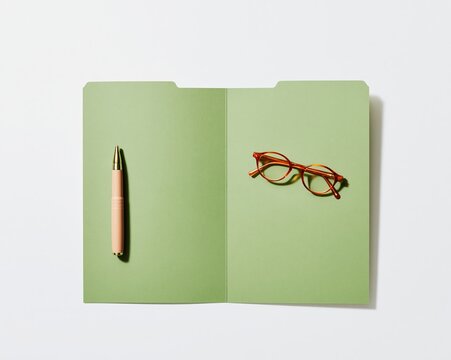 Worn card document folder with softened edges, a thick pen and reading glasses on a clean white background for household admin and mockup
