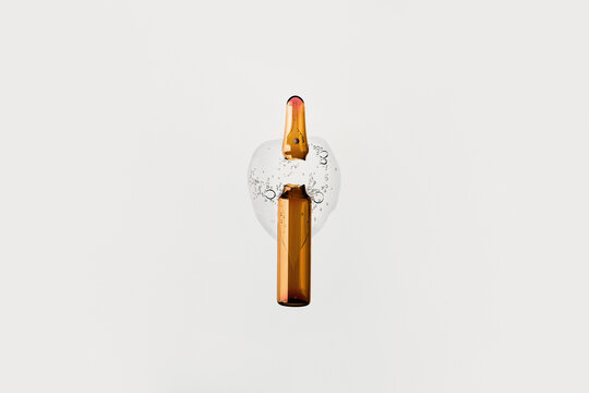 Amber ampoule broken releasing cosmetic serum liquid with bubbles