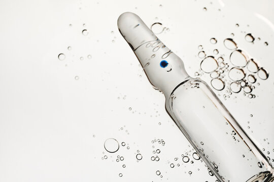 Clear glass ampoule containing liquid and blue dot, surrounded by various size bubbles