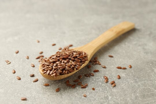 Flax seeds in spoon on grey table, closeup
