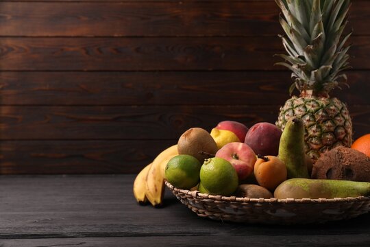 Different fresh fruits in wicker basket on black wooden table, closeup. Space for text