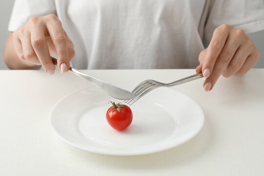 Anorexia concept. Woman refusing plate with tomato at white table, closeup