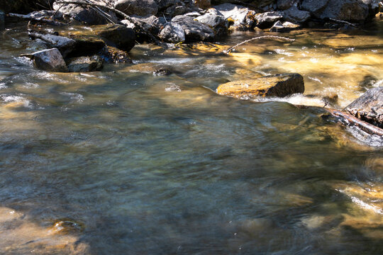 Clear flowing stream over sunlit rocks in natural outdoor setting