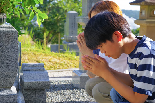 墓前で合掌する母親と子どもたち
