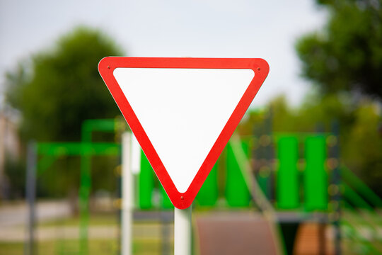 Inverted triangular yield sign with a red border against a green and blurry background.