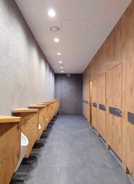 Interior view of a modern commercial restroom featuring warm wooden wall panelling, minimalist urinal dividers, slate-effect flooring, textured walls, and recessed architectural lighting.
