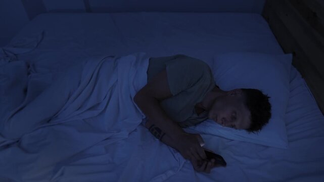 Man compulsively scrolling smartphone in bed at night, struggling with digital addiction, doomscrolling and inability to stop screen time