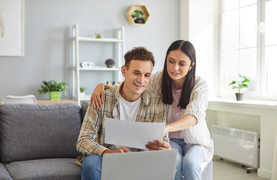Young married couple man and woman working with finances, doing their family budget paperwork, looking through taxation documents, using laptop computer, paying domestic bills online