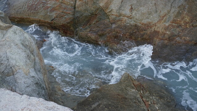 Frothy white ocean waves surging through a narrow channel between wet granite rocks.