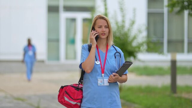 Female paramedic in scrubs talking on the phone outside a hospital