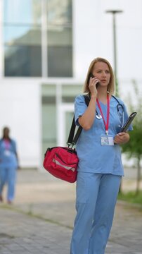 Female paramedic wearing scrubs talking on the phone outside a hospital