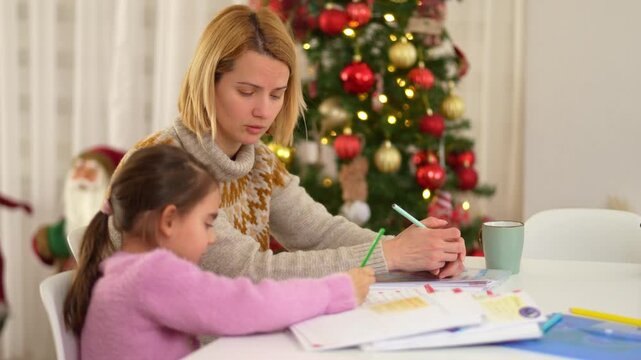 Mother helping daughter with homework during Christmas holidays at home