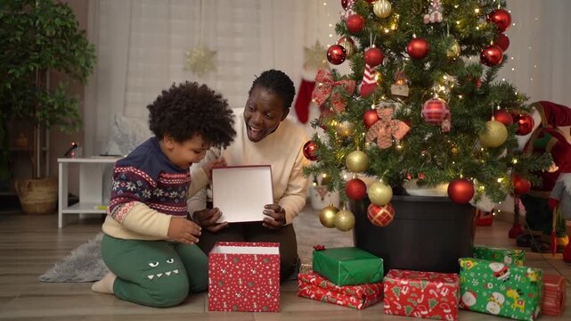 Black mother and her son opening Christmas present near the tree