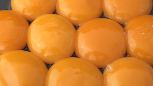 Close-up of bright orange egg yolks arranged in a grid, resting in a dark tray with liquid pooling between them.