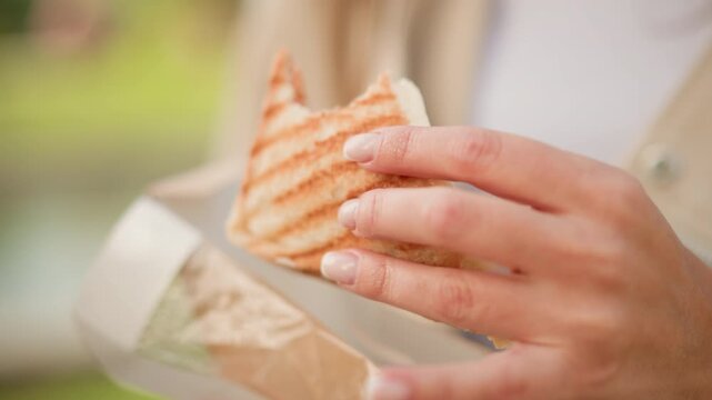 Close up of woman holding and eating open faced sandwich with visible meat filling. subject hand gently manipulates food revealing texture details like toasted bread grill marks