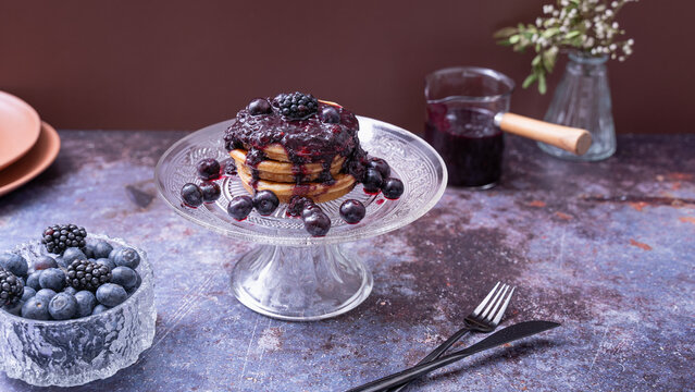 Berry Pancakes on Glass Cake StandHomemade pancakes topped with berry compote fresh blueberries blackberries and figs served on an elegant glass cake stand