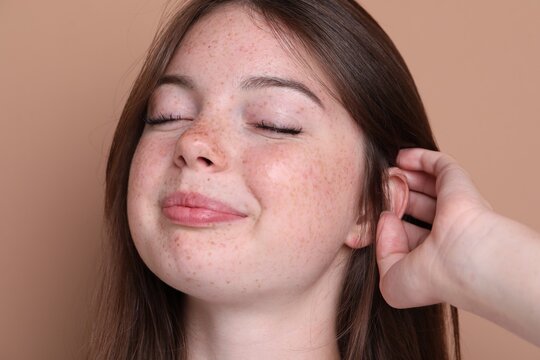 Beautiful teenage girl with freckles on light brown background, closeup