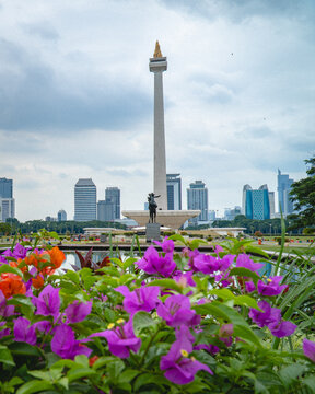 Jakarta, Indonesia - August 29, 2026: The National Monument, or Monas, rises above a colorful flower garden with the Jakarta city skyline in the background under a cloudy sky.