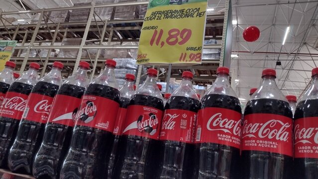 ITABIRA, BRAZIL - AUGUST 26, 2026: Coca-Cola plastic bottles on a wholesale market shelf under a yellow price offer sign