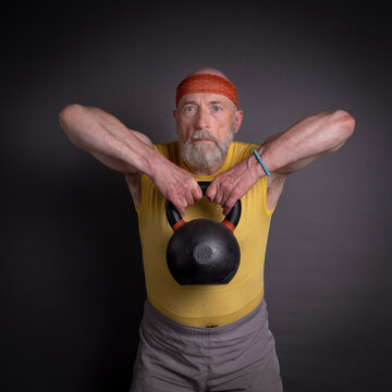 athletic senior man is training with a heavy iron kettlebell, fitness over 60 and 70 concept
