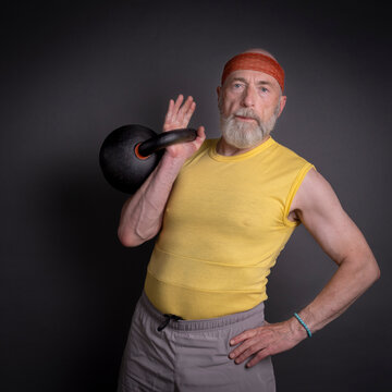 athletic senior man is training with a heavy iron kettlebell, fitness over 60 and 70 concept