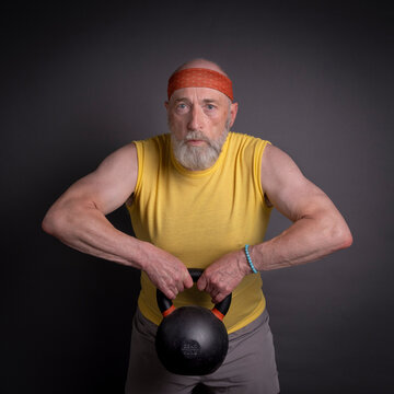 athletic senior man is training with a heavy iron kettlebell, fitness over 60 and 70 concept