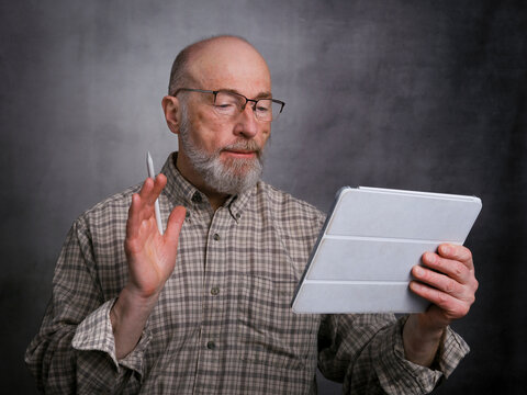 casual portrait of bald, bearded senior man working on a digital tablet with electronic pencil