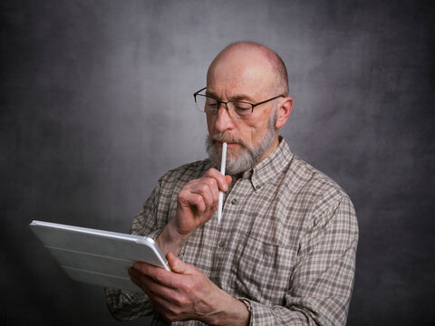 casual portrait of bald, bearded senior man working on a digital tablet with electronic pencil
