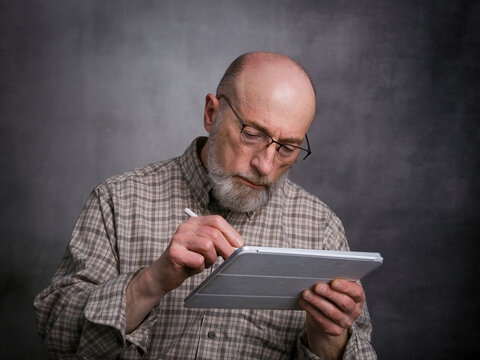 casual portrait of bald, bearded senior man working on a digital tablet with electronic pencil