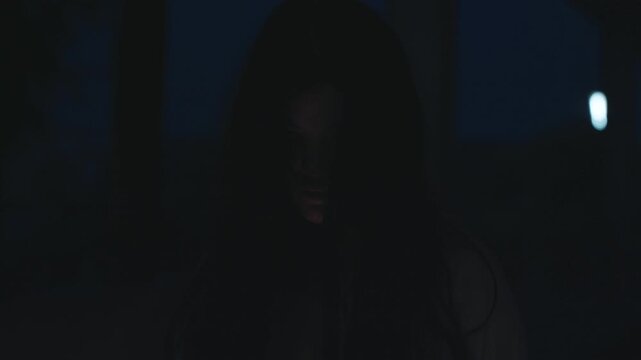 Scary halloween ghost emerges from black night, pale face with dramatic makeup, dark costume, dead eyes, psychopath like gaze, chilling character for horror themed celebration night party.