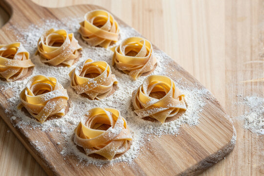 Raw handmade tagliatelle pasta nests on wooden board with flour