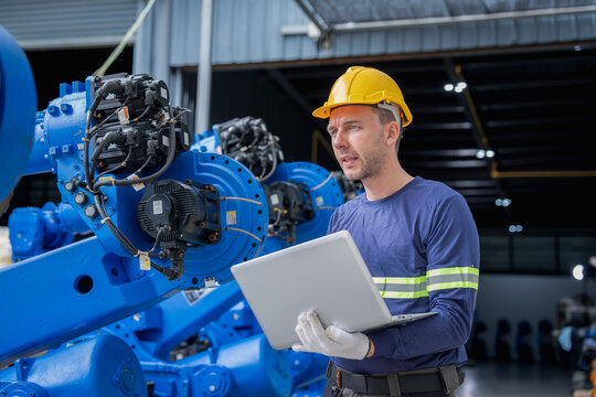 Engineer overseeing robotic automation technology in a contemporary industrial setting while using a laptop