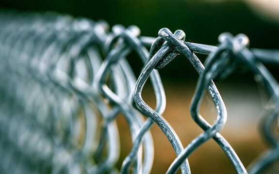 Close up of metal chain link fence with blurred green background