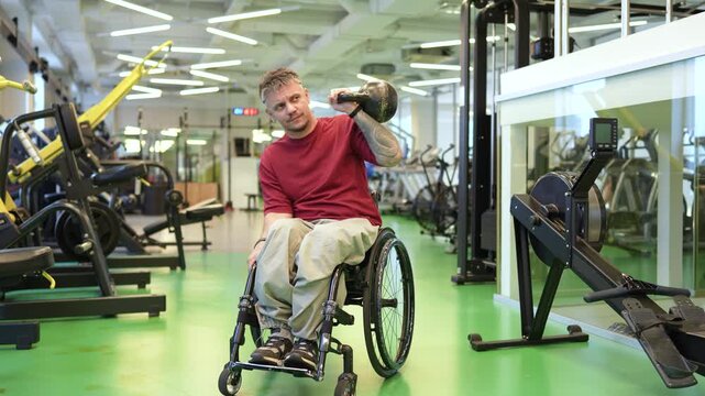 Disciplined focused man in wheelchair working out in gym at training and lifting kettlebell, confident male athlete building core and back muscles with heavy weights, strengthening upper body